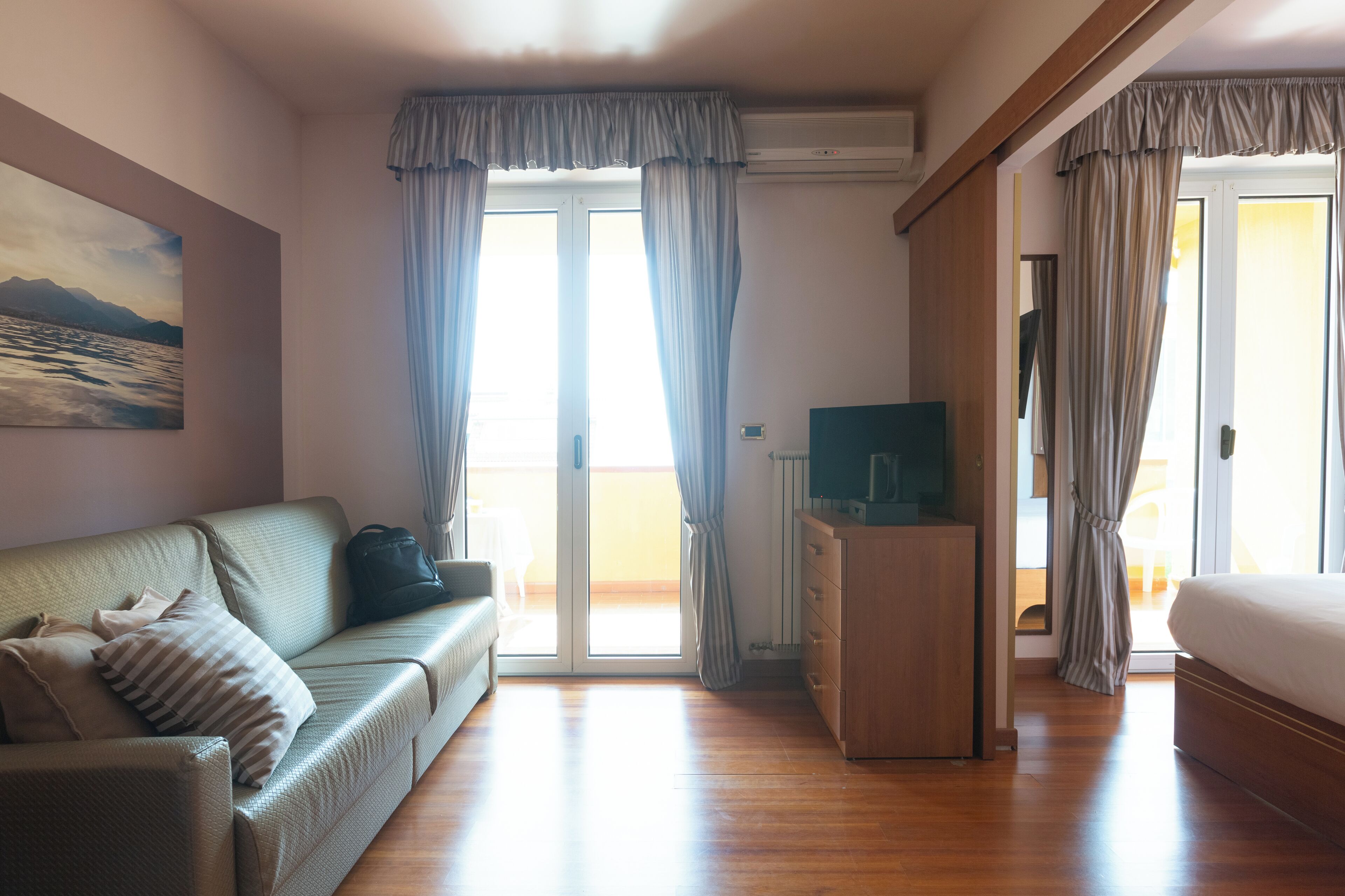 A room with a sofa, a TV, a bed, and a sliding glass door leading to a balcony.