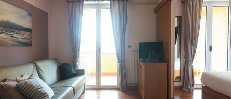 A room with a sofa, a TV, a bed, and a sliding glass door leading to a balcony.
