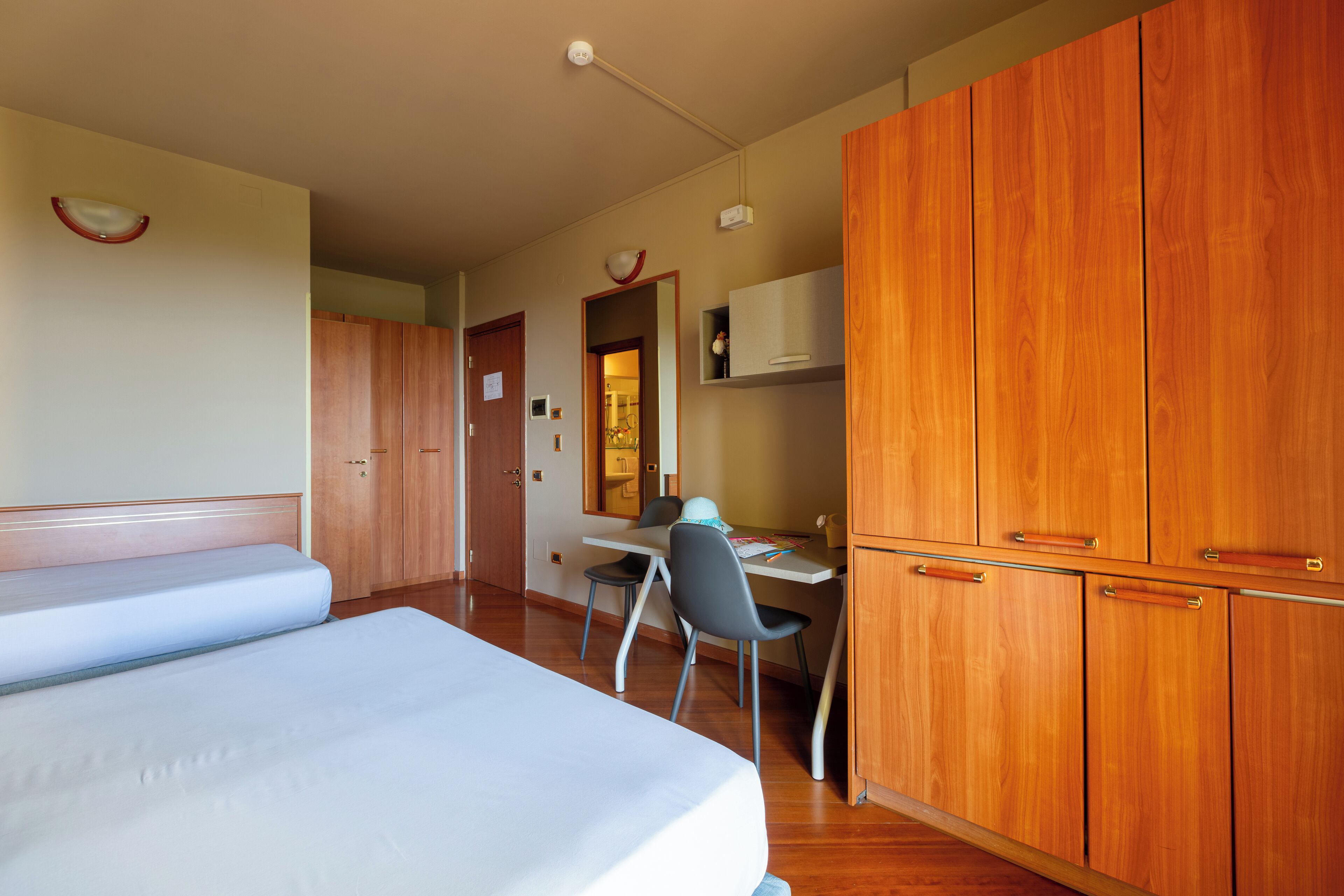 Una camera d'albergo con un letto, una scrivania, una sedia, un armadio e uno specchio.