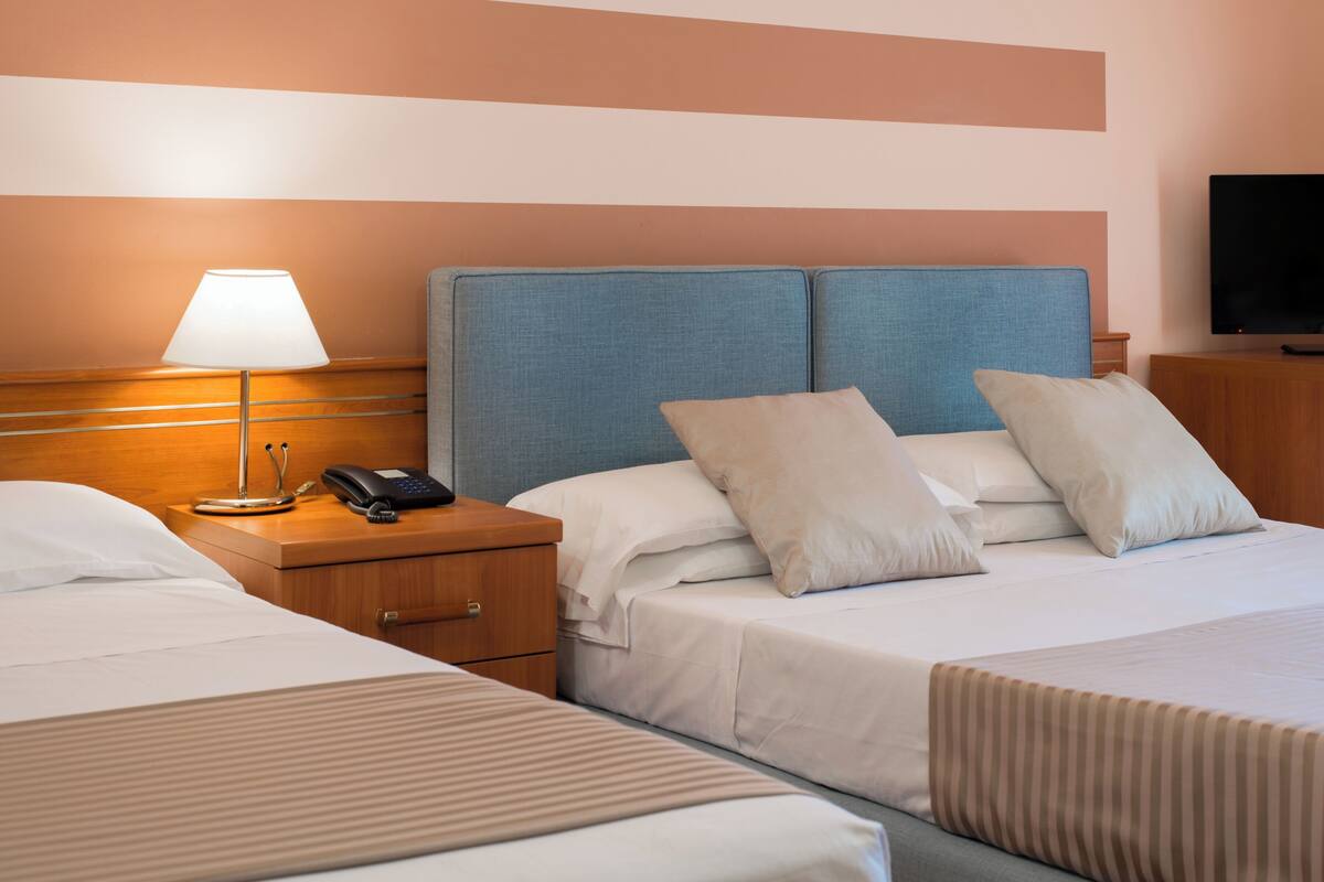 A hotel room with two beds, a bedside table with a lamp, a phone, and a TV.