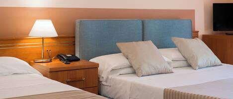 A hotel room with two beds, a bedside table with a lamp, a phone, and a TV.