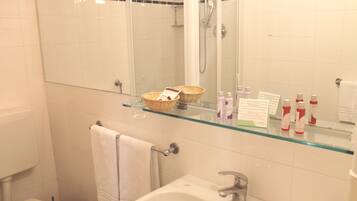 Een badkamer met een glazen plankje met toiletartikelen, een witte wastafel en een glazen douchecabine.