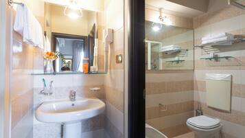 A bathroom with a sink, mirror, toilet, and glass shelves with towels.