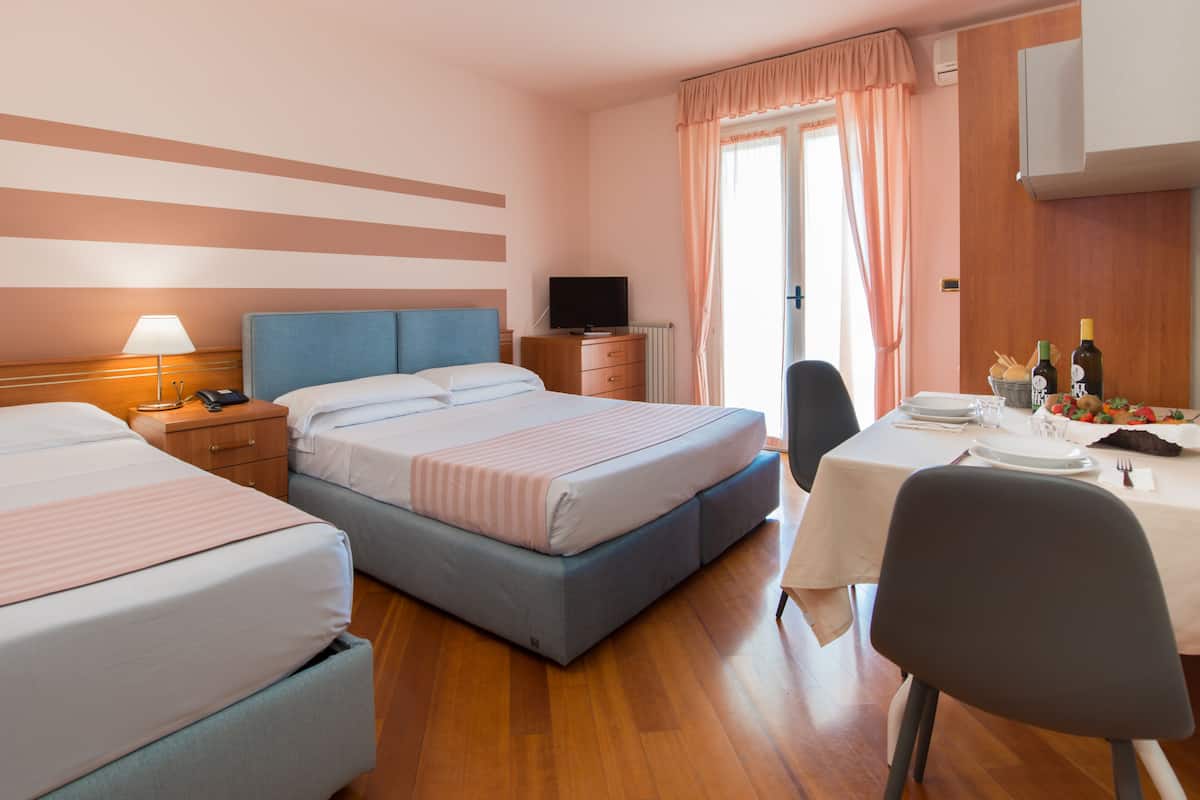 A hotel room with two beds, a TV, a dining table with chairs, and a window with curtains.