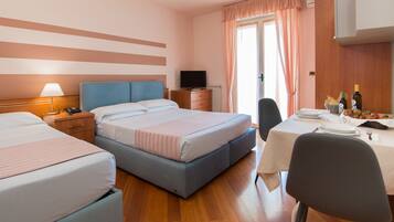 Quarto de hotel com duas camas, televisão, mesa de jantar com cadeiras e janela com cortinas.