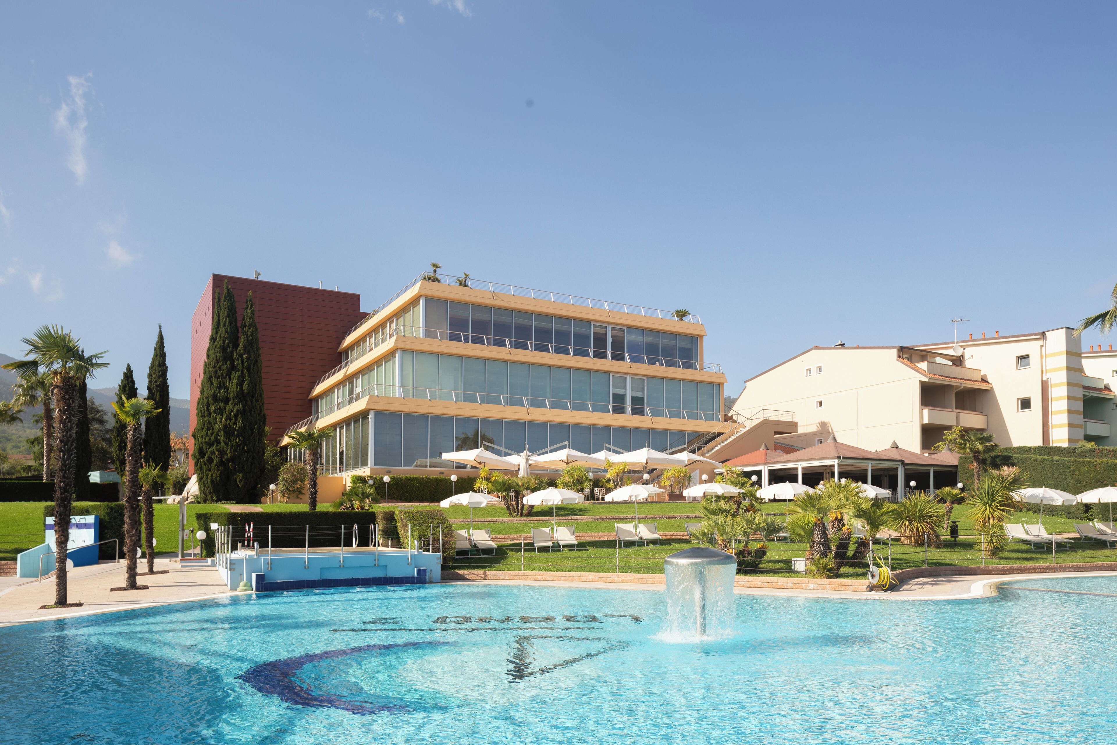 Ein Schwimmbecken mit Liegestühlen und Sonnenschirmen, umgeben von Gebäuden und Palmen.