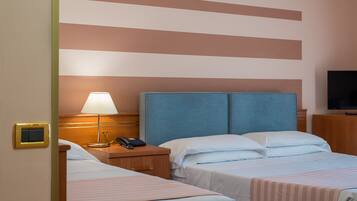 Habitación de hotel con dos camas, una mesita de noche con lámpara, un televisor y un cabecero de madera.