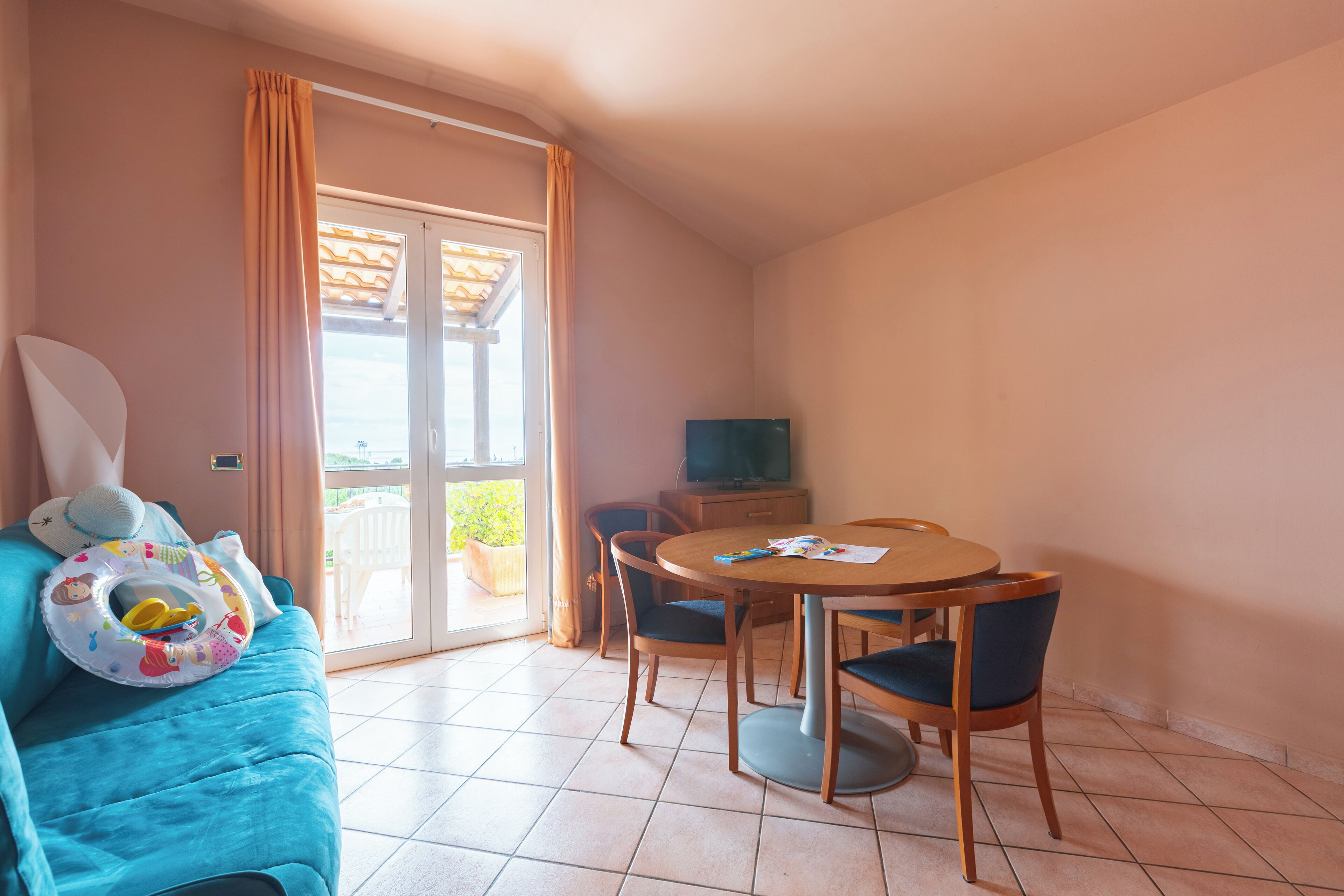 A room with a blue sofa, a dining table with chairs, a television, and a sliding glass door leading to an outdoor area.