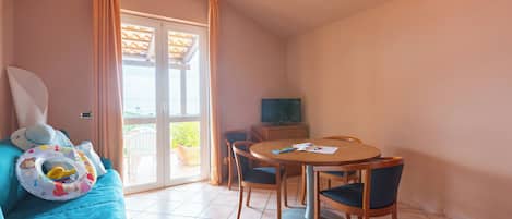 A room with a blue sofa, a dining table with chairs, a television, and a sliding glass door leading to an outdoor area.