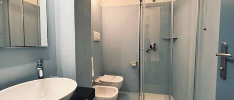 Een moderne badkamer met een groot wit wastafelmeubel, een toilet en een douche met glazen wanden.