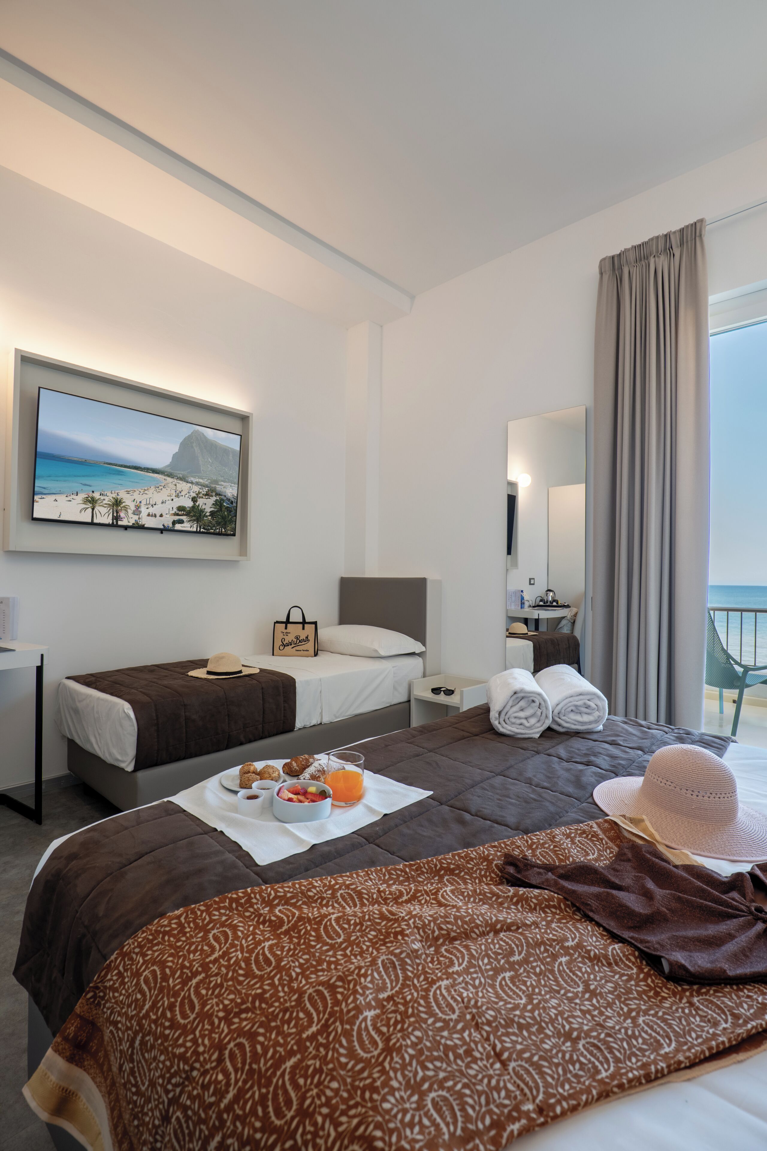 A hotel room with a bed, a desk, a chair, a TV, and a balcony with a view.