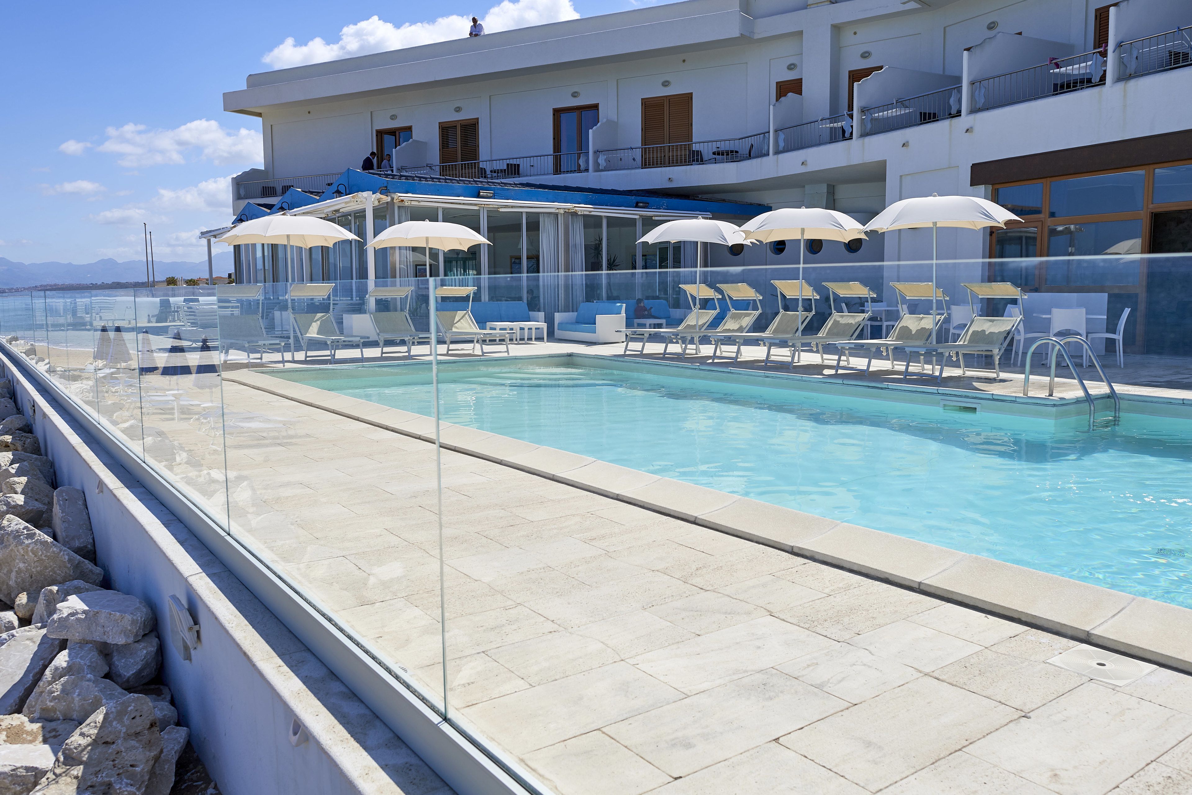 Un espace aménagé au bord de la piscine, avec des chaises longues et des parasols, une piscine à eau claire et un bâtiment doté de balcons.