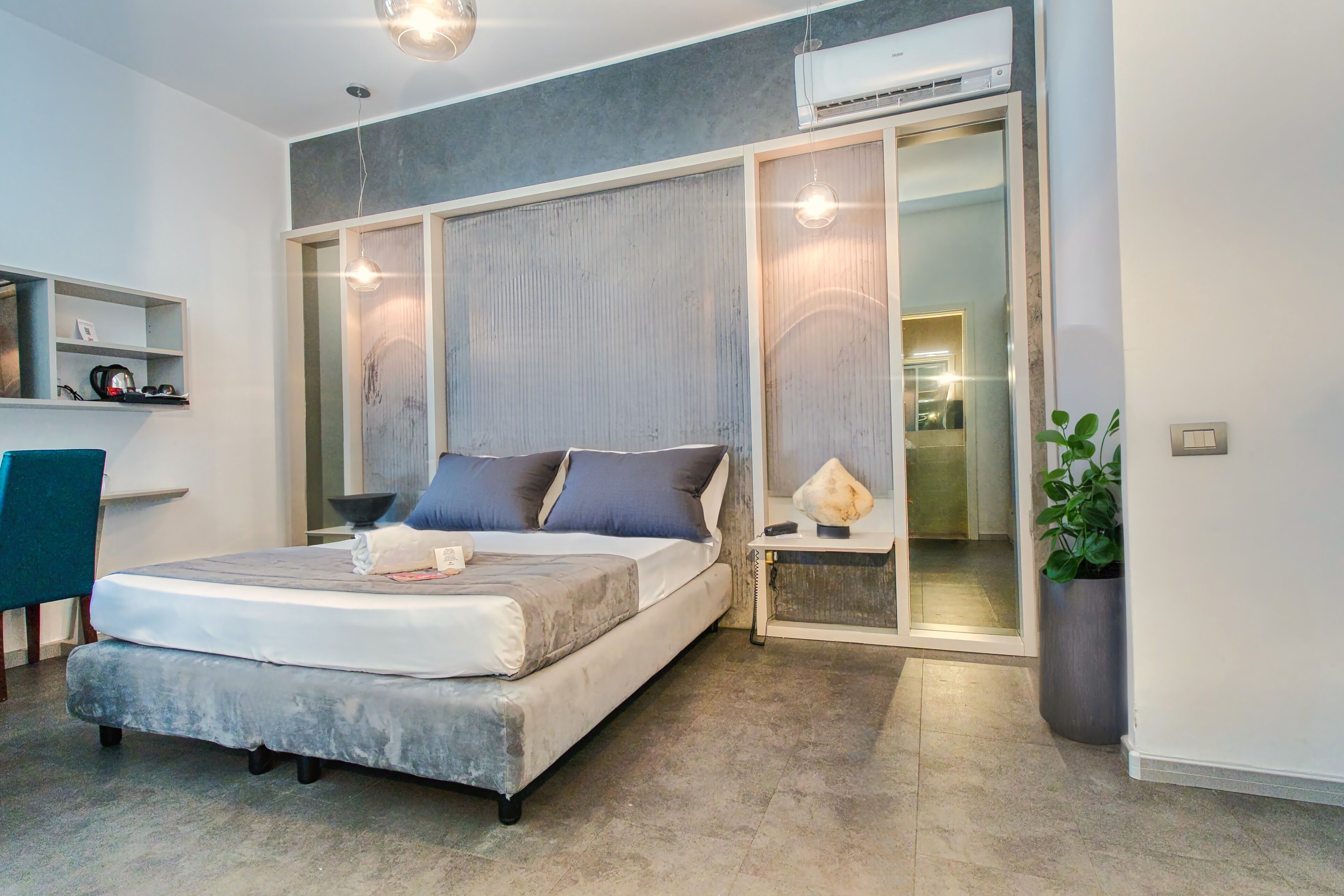 A modern bedroom with a large bed, a bedside table, a mirror, and an air conditioning unit.