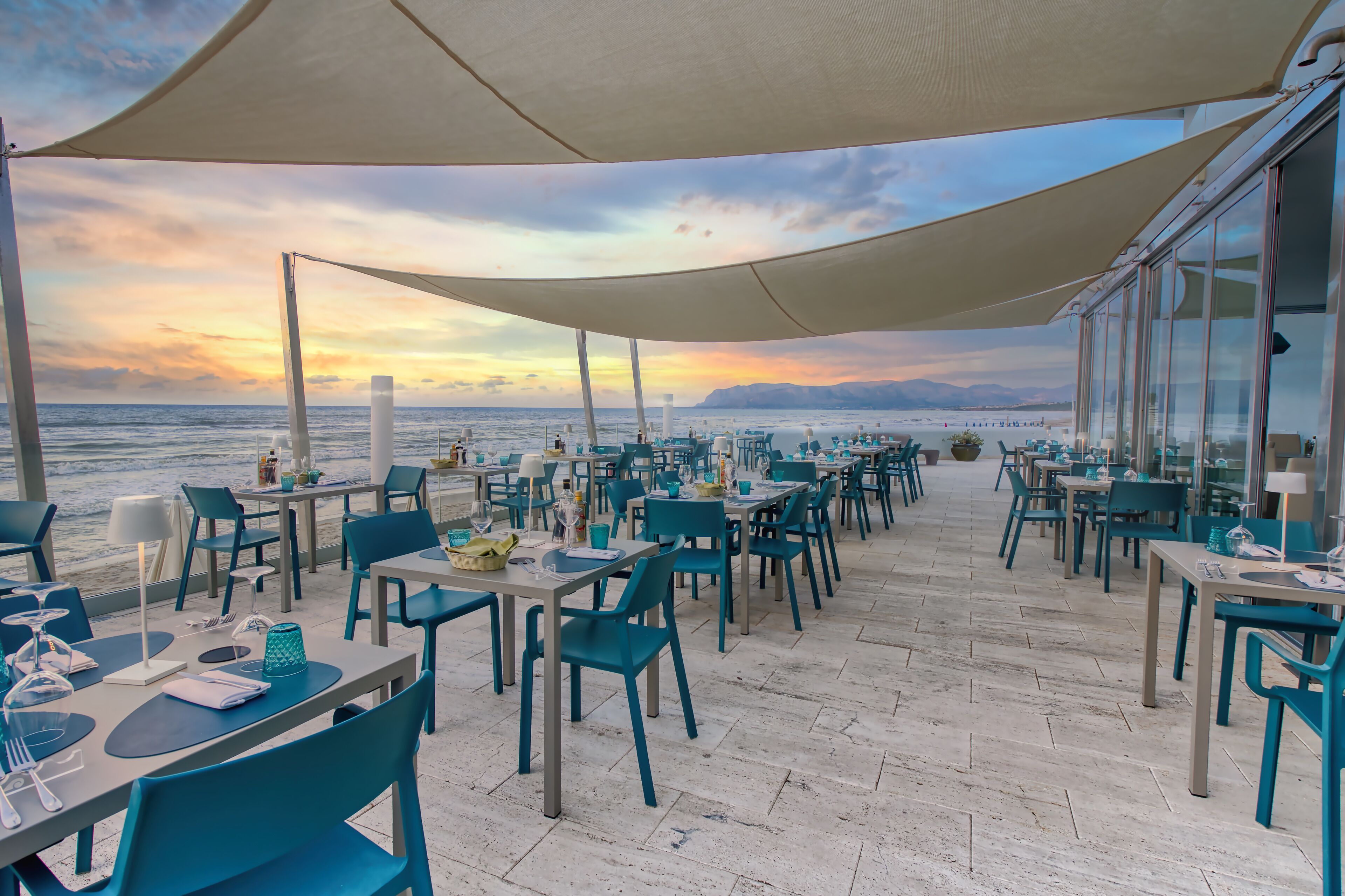 A seaside restaurant with outdoor seating, tables, and chairs, overlooking the ocean.
