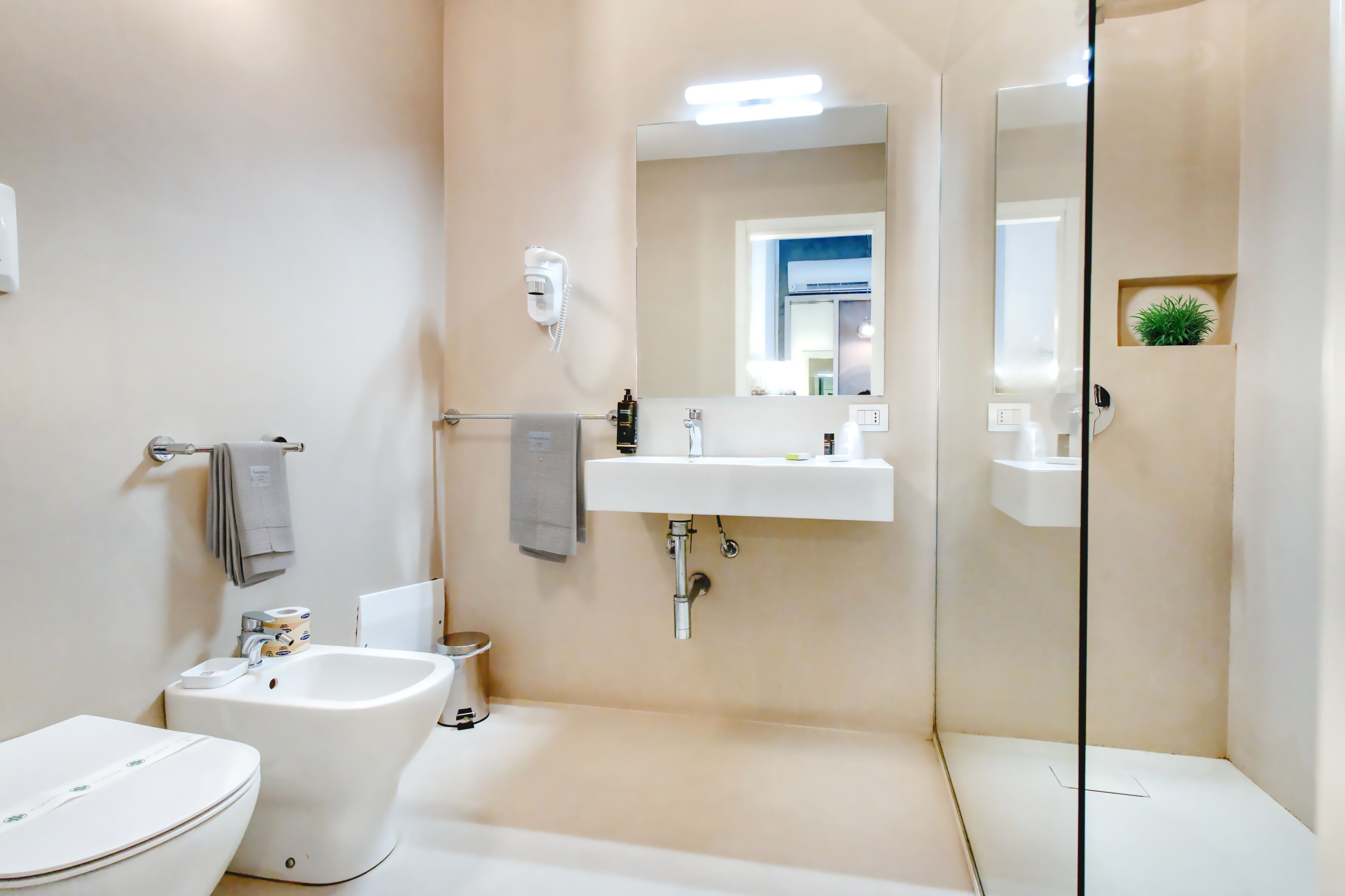 Een moderne badkamer met toilet, bidet, wastafel en een douchecabine met glazen wanden.