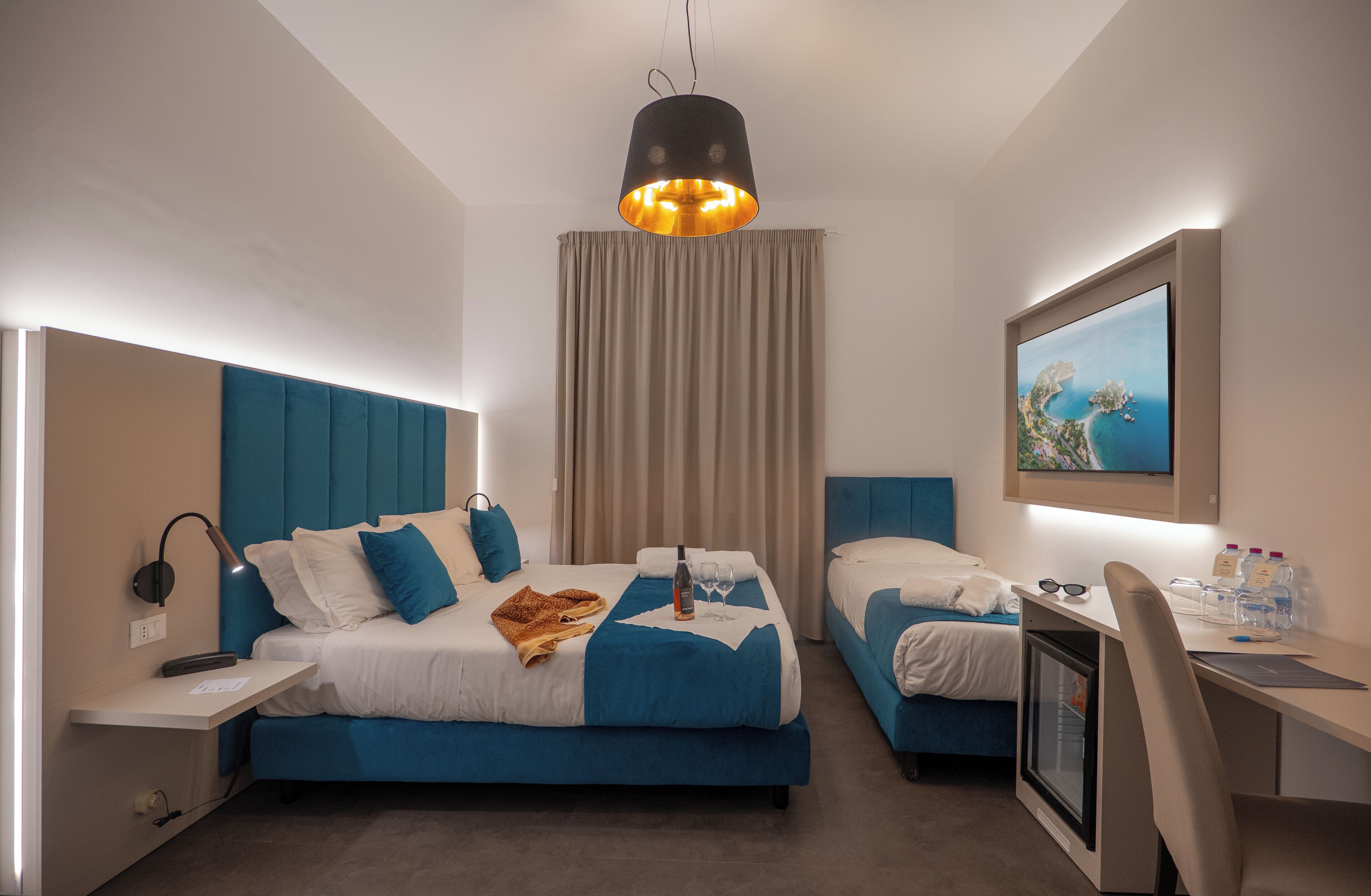 Una habitación de hotel moderna con cama, escritorio, silla, televisor y ventana con cortinas.
