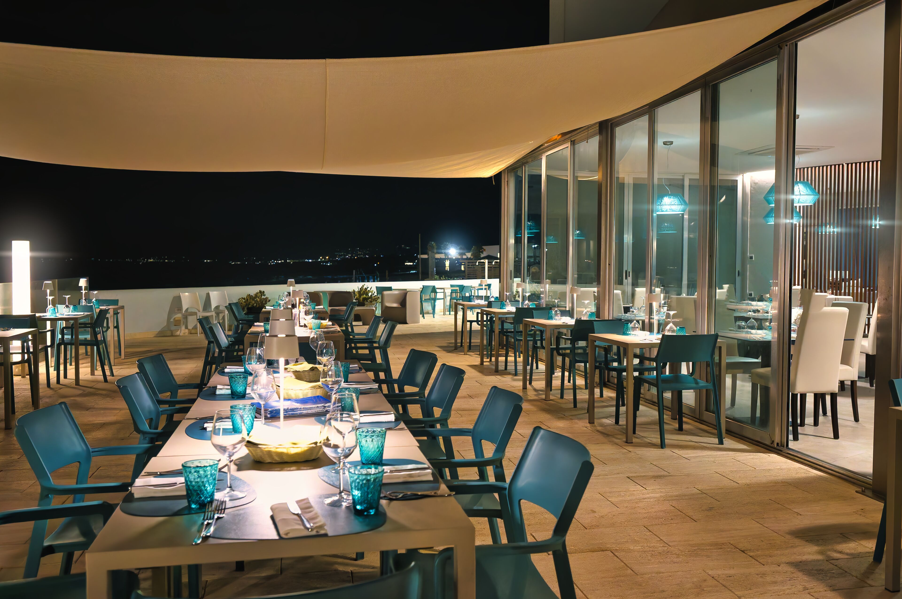 An outdoor dining area with tables and chairs, large windows, and a view of the night sky.