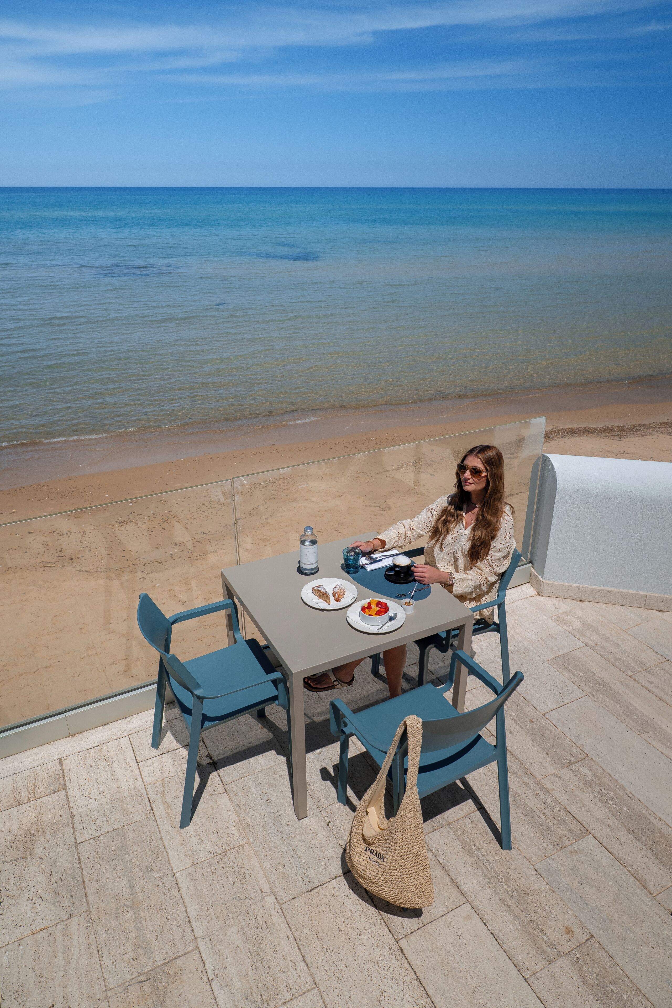 Una persona sentada a una mesa con vistas al mar, una silla de playa y una sombrilla.