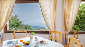A table set for breakfast with a scenic view, including a plate with croissants, fruits, and a cup of coffee. - Hotel San Trano (Luogosanto)