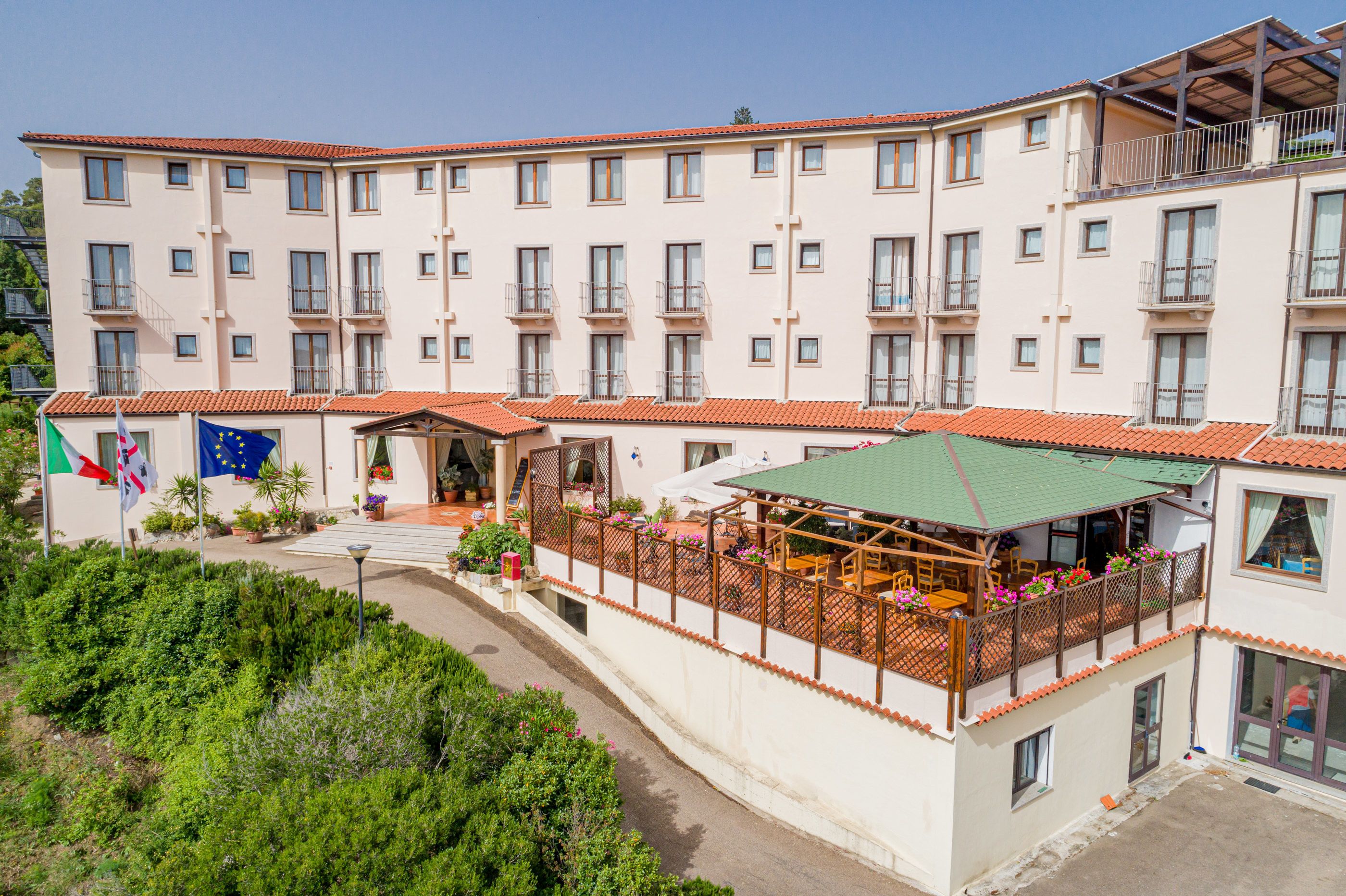 Un hotel a più piani con balconi, una zona relax all'aperto coperta e una bandiera che indica l'appartenenza all'Unione Europea.