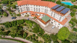 A multi-story hotel with a red-tiled roof, solar panels, and a swimming pool. - Hotel San Trano (Luogosanto)