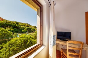 Ein Zimmer mit Fenster und Blick auf eine üppige, grüne Landschaft, einem Holztisch mit Fernseher und einem Sessel.
