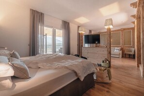 A bedroom with a large bed, a TV, a wooden wardrobe, and a balcony. - Cristallo Levico Terme (Levico Terme)