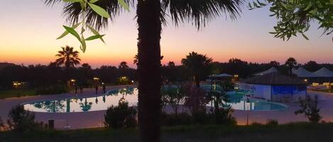A resort pool area with palm trees and a sunset in the background.