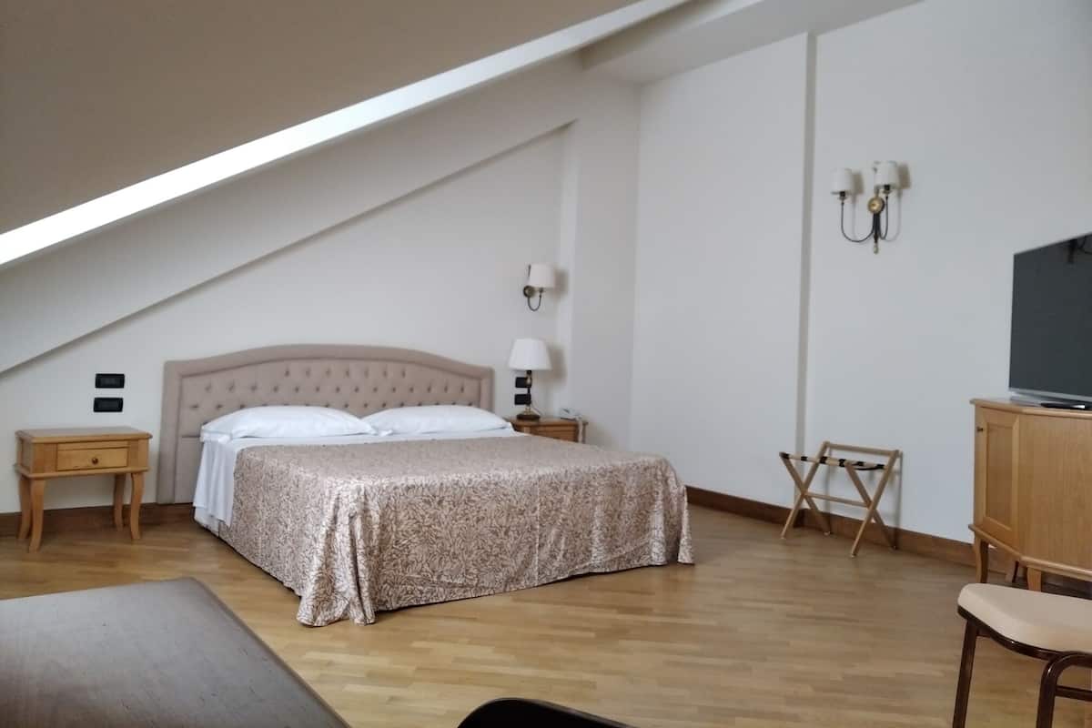A bedroom with a bed, bedside tables, a TV, and a desk.