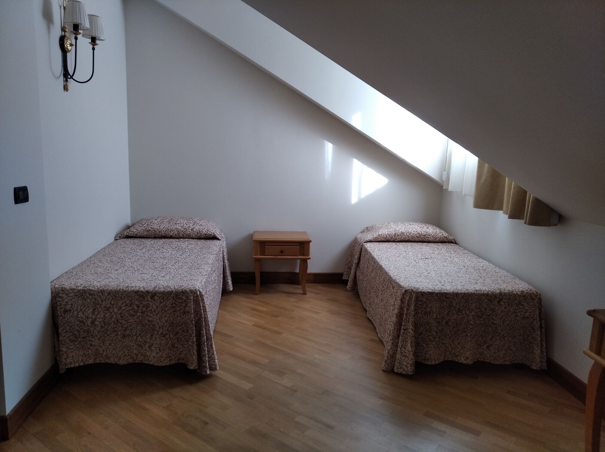 Une petite pièce simple, avec deux lits, une table de chevet et un plafond en pente.