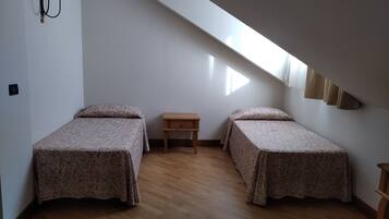 Une petite pièce simple, avec deux lits, une table de chevet et un plafond en pente.