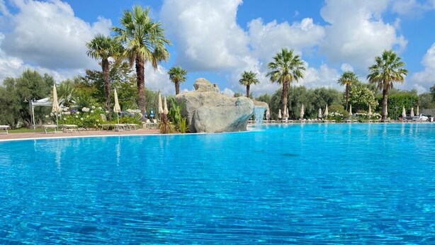 Una piscina azul cristalina rodeada de palmeras y una gran formación rocosa.