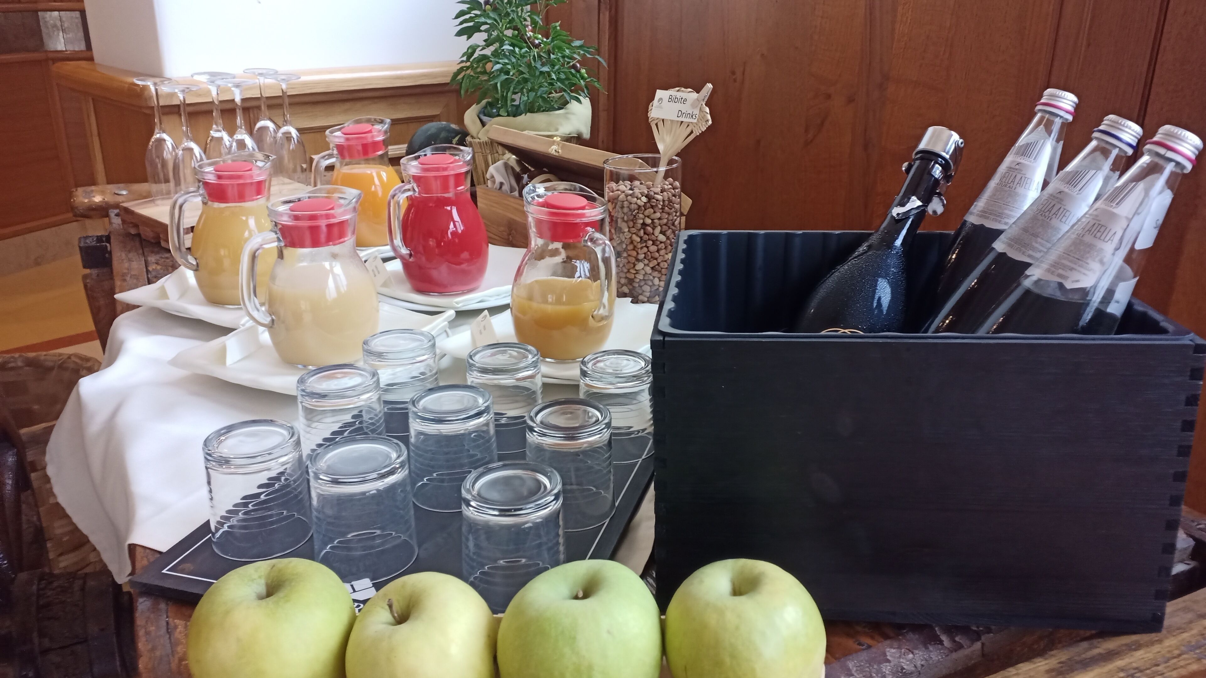 Una mesa con diferentes bebidas, incluyendo botellas y vasos, y varias manzanas.