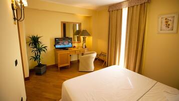 Ein Hotelzimmer mit Bett, Schreibtisch, Stuhl, Fernseher und einer Zimmerpflanze.
