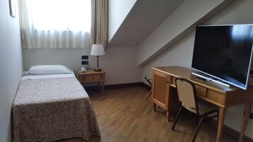 Una stanza piccola e ordinata con un letto, una scrivania, una sedia, una televisione e una lampada.