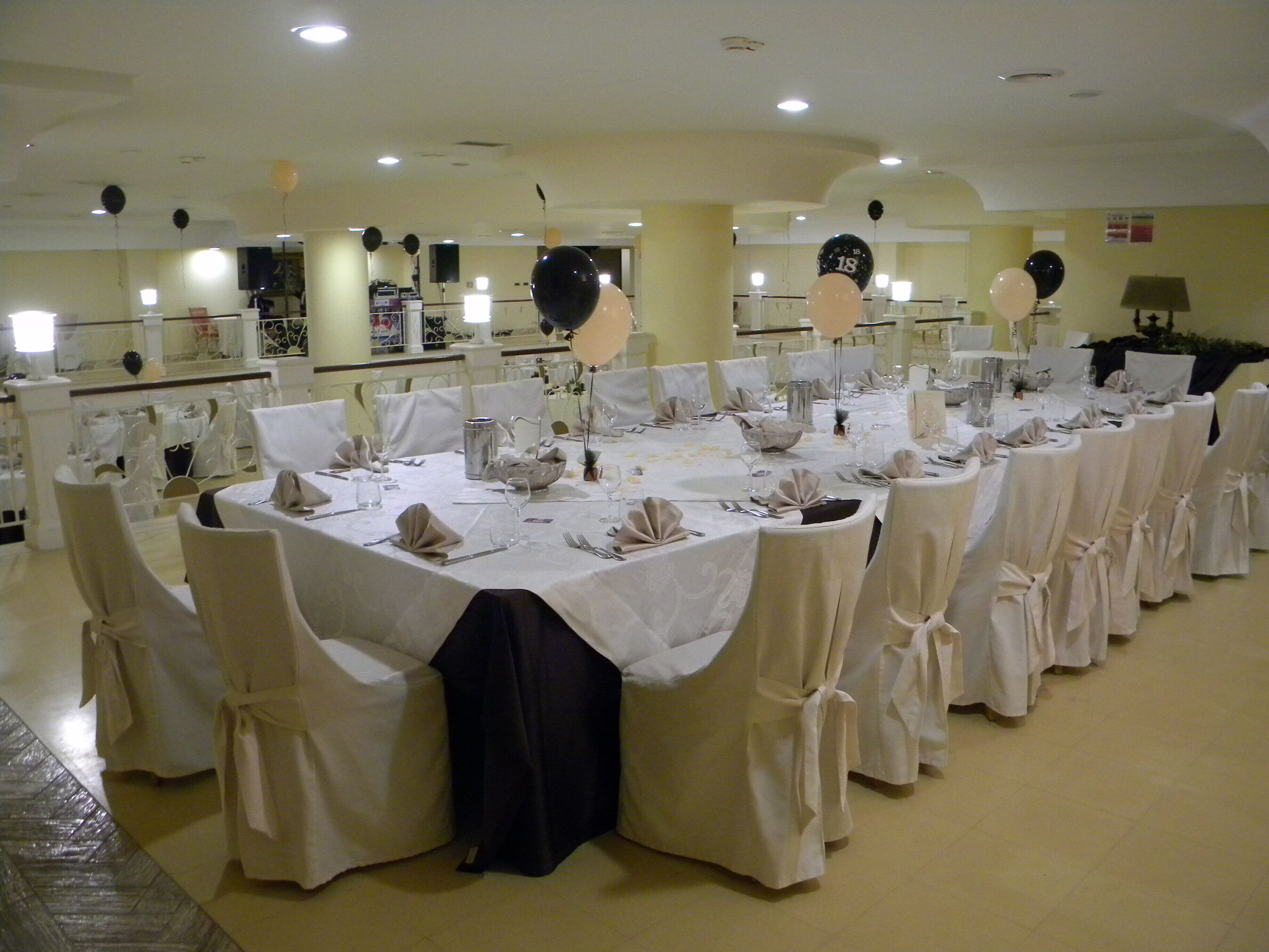 Una sala da banchetto con tavoli rotondi apparecchiati per un evento formale, con tovaglie bianche e sedie con copri-sedile legati.