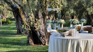 Un espacio de comedor al aire libre con una mesa redonda, mantel blanco y centros de mesa florales.