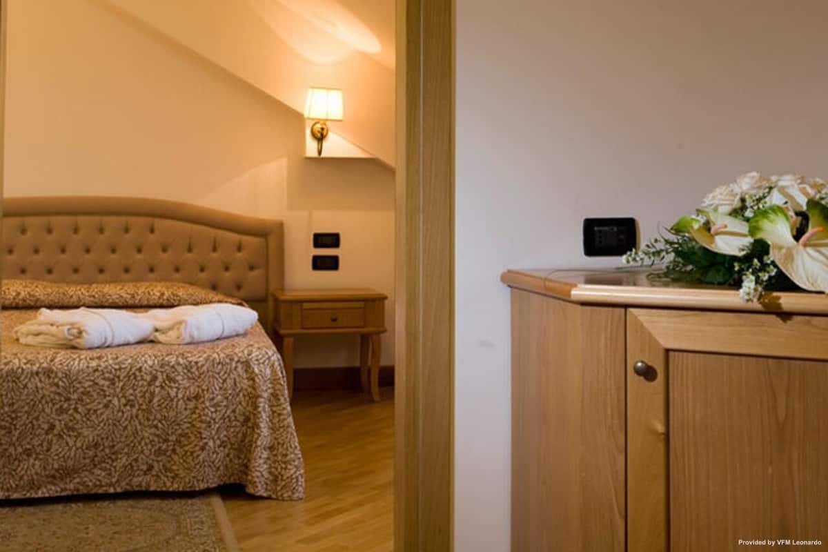 A bedroom with a bed, bedside table, lamp, and a cabinet with a floral arrangement.