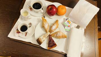 Un plateau de petit-déjeuner avec des croissants, une pomme rouge, une orange et deux tasses de café, posé sur une table en bois.