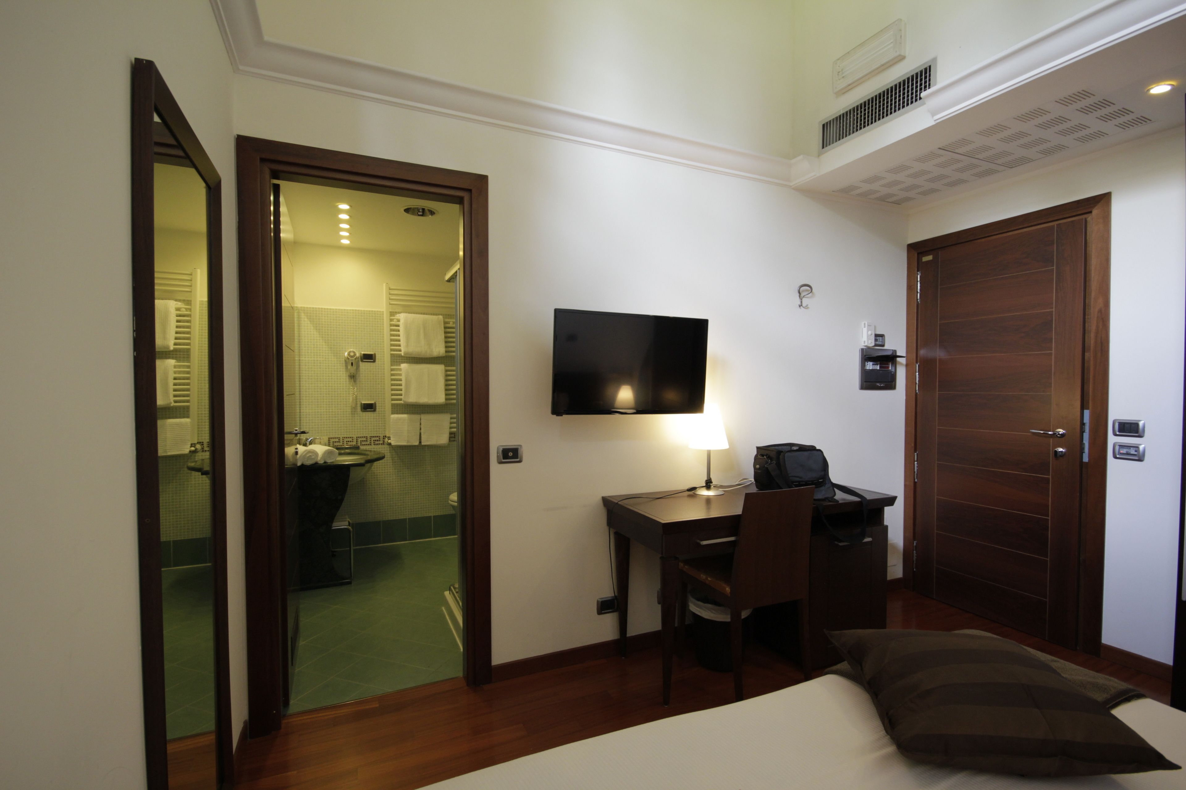 Habitación de hotel con cama, escritorio con silla, televisión y puerta que da al baño.