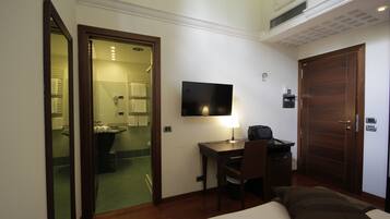 A hotel room with a bed, a desk with a chair, a television, and a door leading to a bathroom.