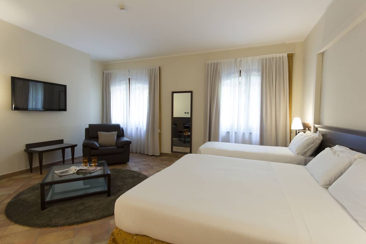 A hotel room with a bed, a sofa, a TV, a desk, and a mirror.