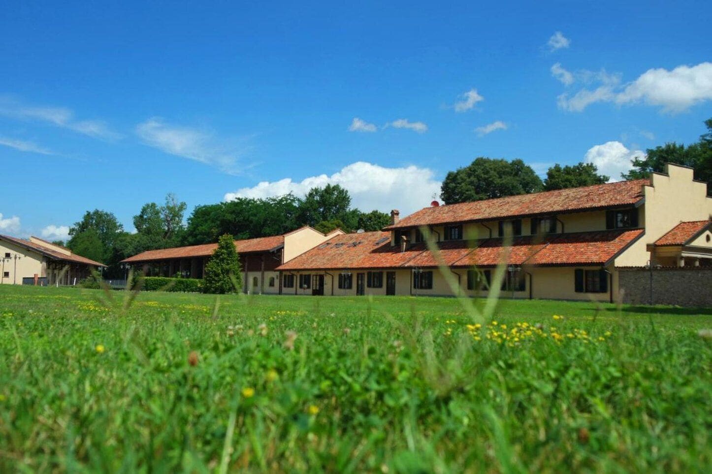 Eine Reihe traditioneller Gebäude mit roten Ziegeldächern, eingebettet in ein grünes Feld unter blauem Himmel.