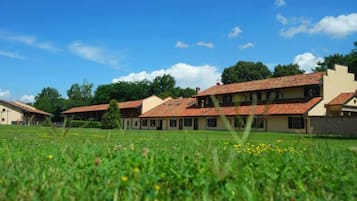 Eine Reihe traditioneller Gebäude mit roten Ziegeldächern, eingebettet in ein grünes Feld unter blauem Himmel.