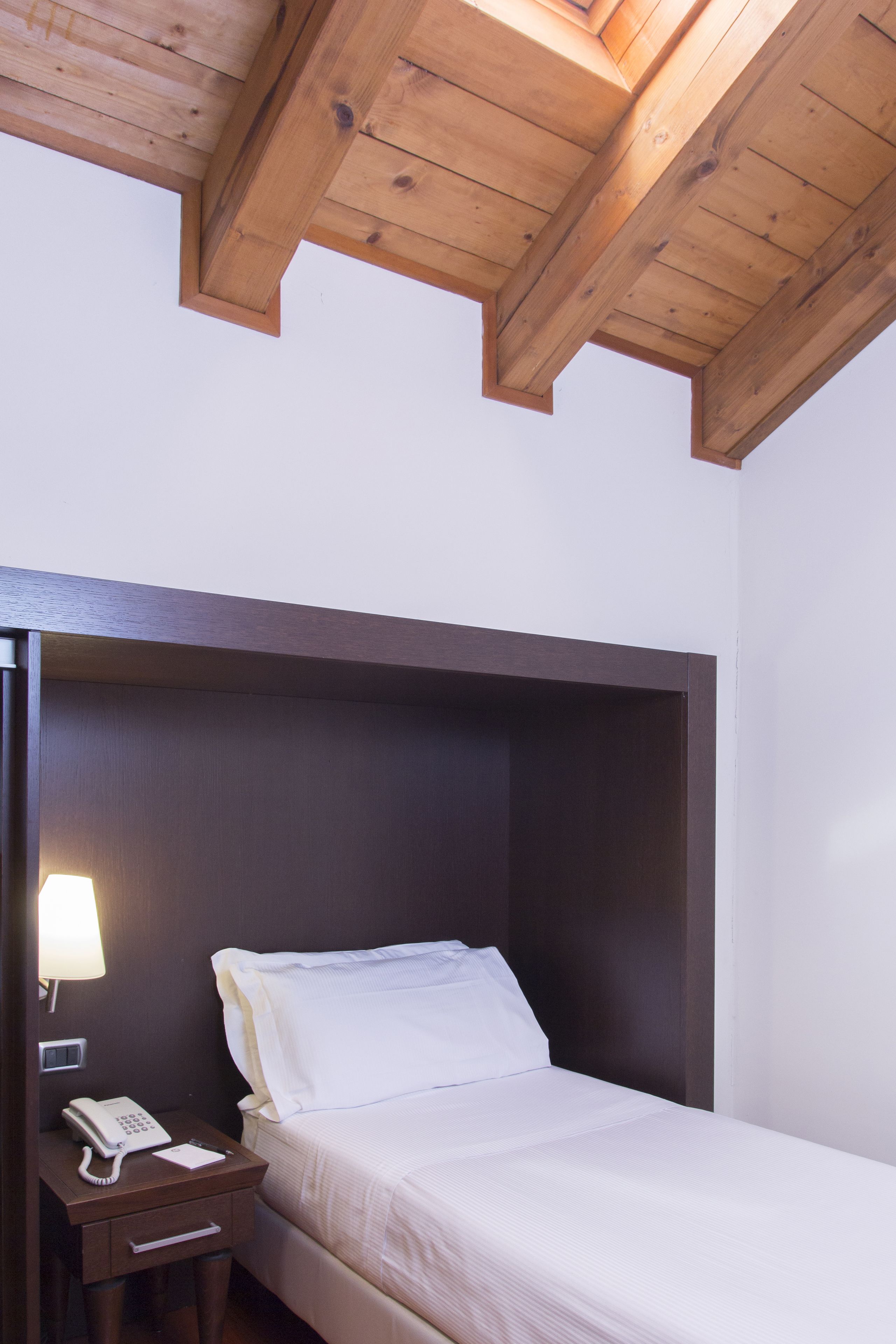 A single bed with a wooden headboard, a bedside table with a lamp, and a telephone.