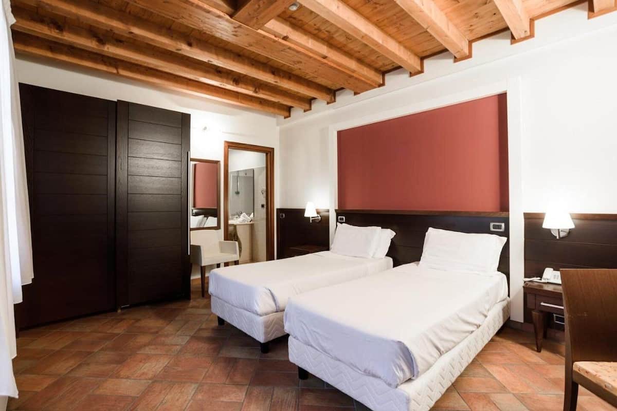 A hotel room with two beds, wooden ceiling beams, a large mirror, and a red accent wall.