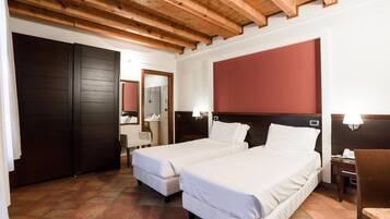 A hotel room with two beds, wooden ceiling beams, a large mirror, and a red accent wall.