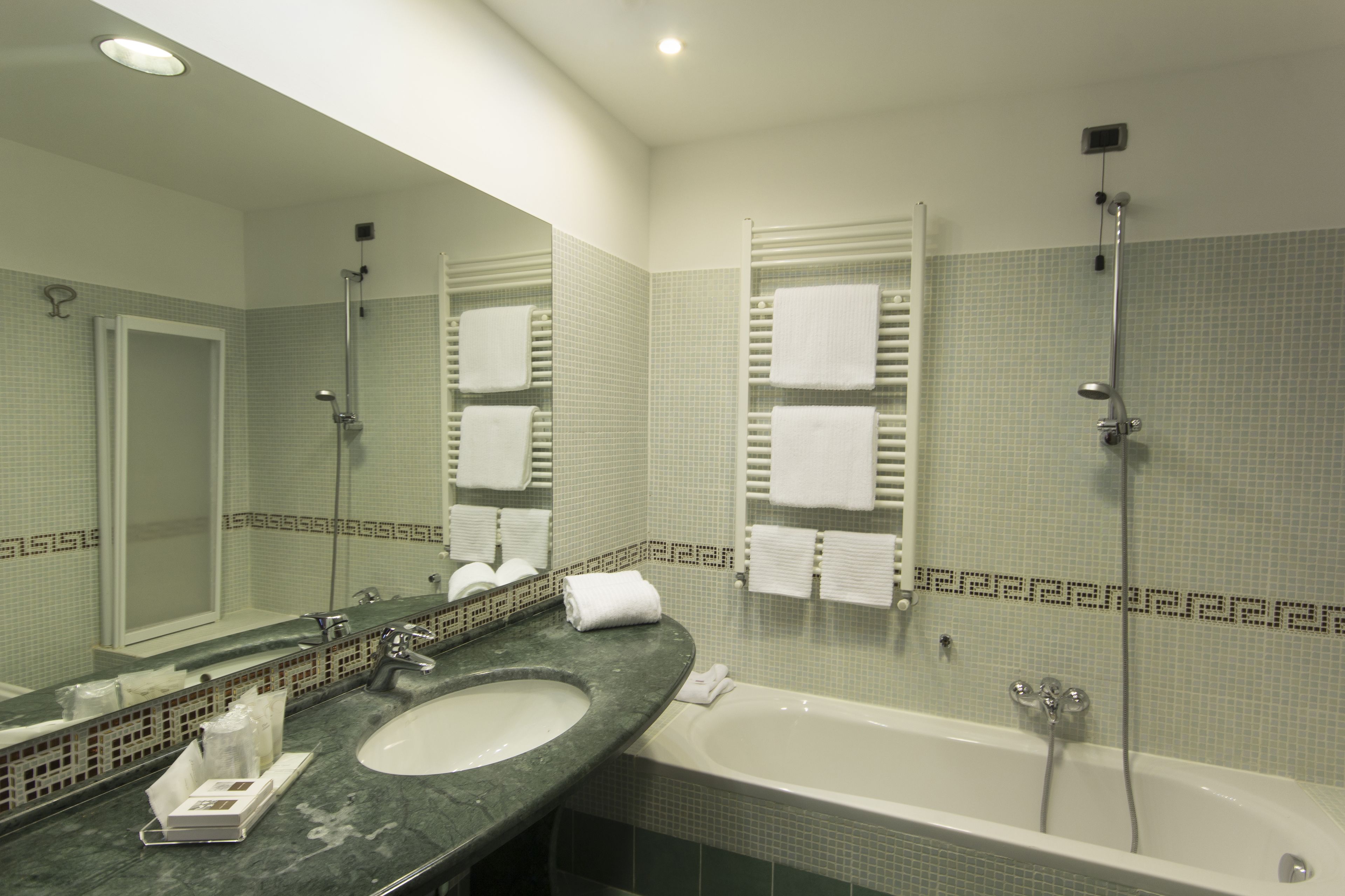 A bathroom with a sink, mirror, and bathtub. There are towels hanging on the wall and a showerhead above the bathtub.