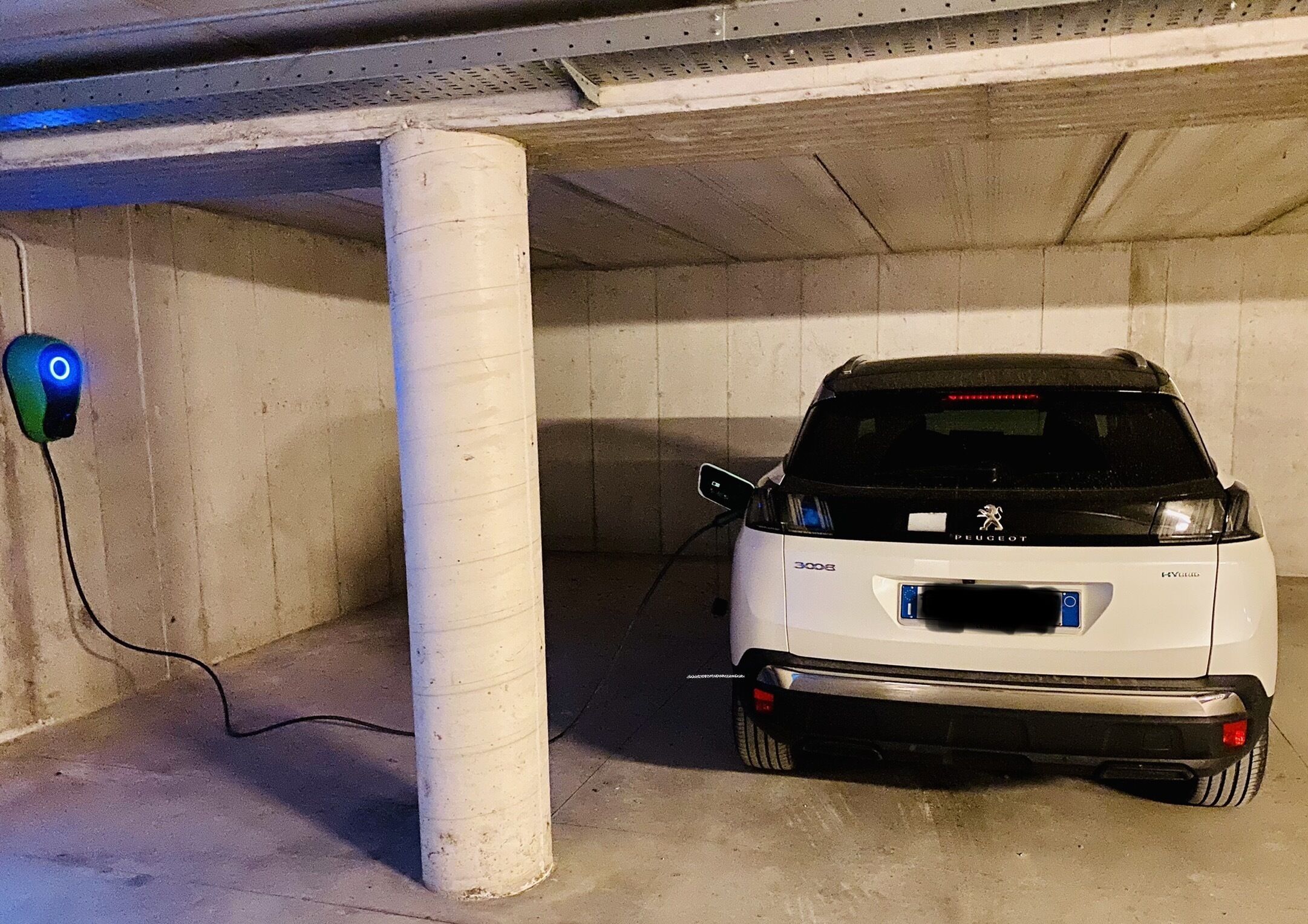 Ein weißes Auto steht in einer Betonparkgarage neben einer Ladestation.