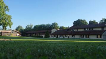 A building with multiple rooms, a lawn, and trees in the background.
